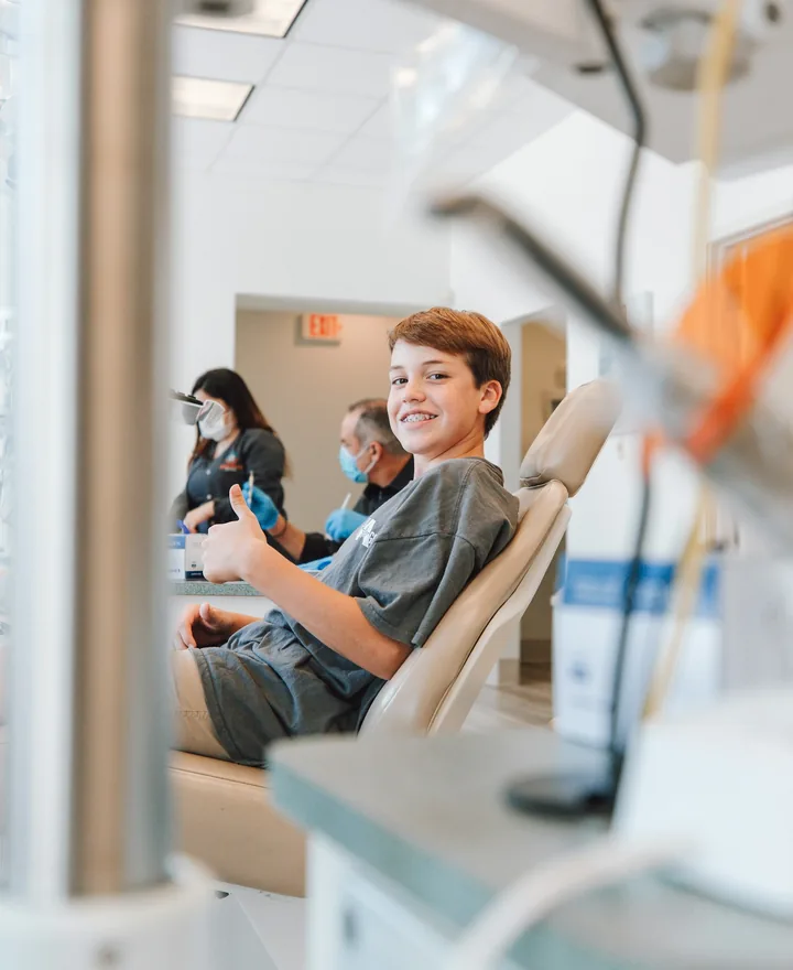 Smiling young patient sitting in a dental chair while a parent waits nearby